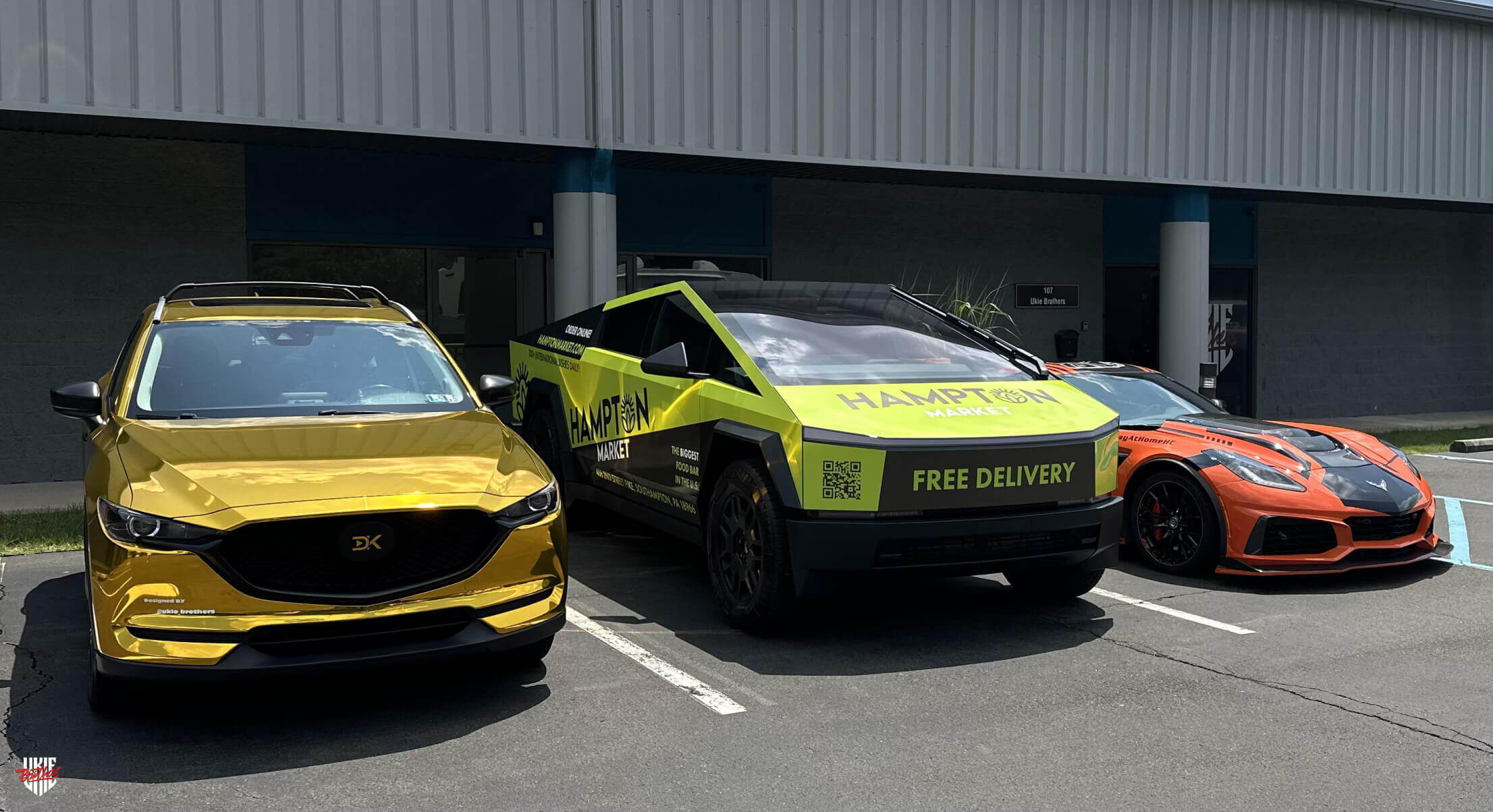 Tesla Cybertruck wrapped in Hampton Market vinyl advertising with 'Free Delivery' promotion, parked alongside a gold-wrapped Mazda and an orange Chevrolet Corvette in front of a commercial building under a sunny sky.